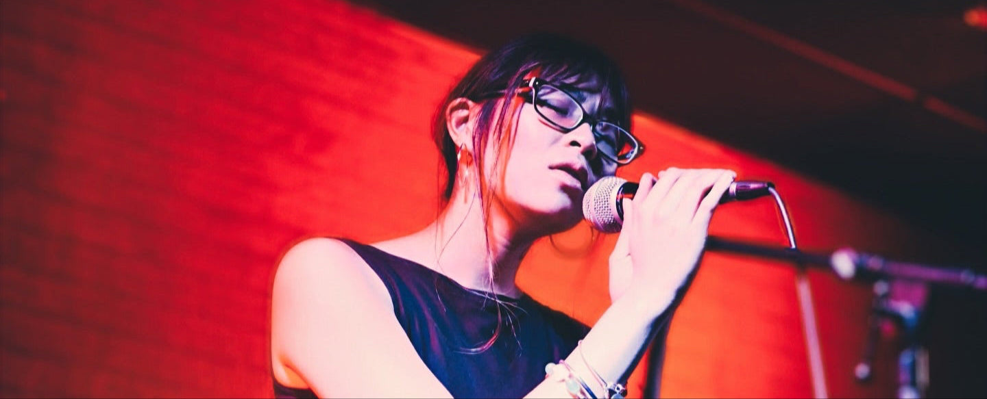 Person singing into a microphone on stage with red lighting